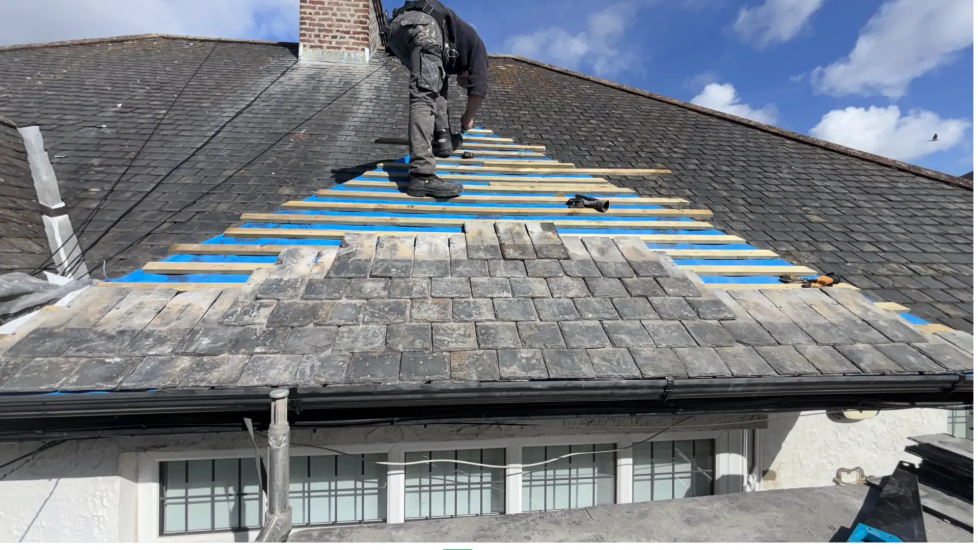 Roofer fitting slates over new battens and blue underlay on a pitched roof